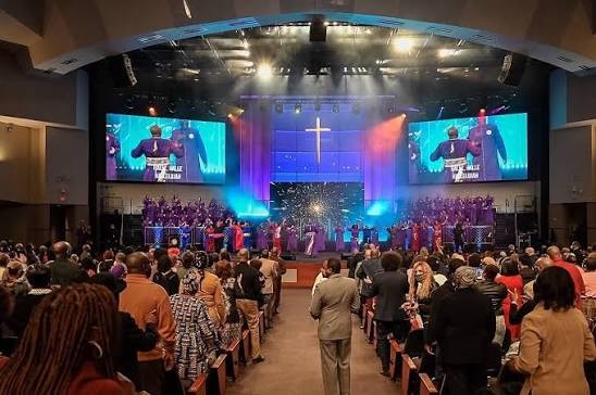 The sanctuary at First Baptist Church of Glenarden during the Anniversary Production: the choir on stage under stage lighting, a full congregation standing