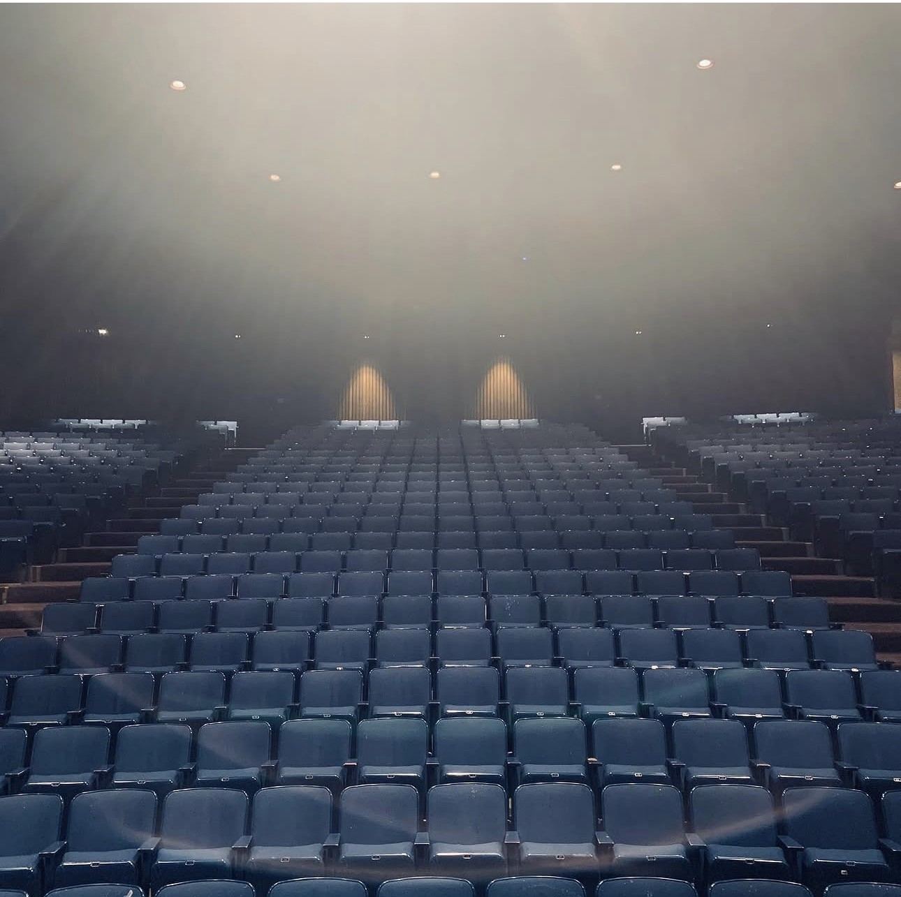 An empty theater house in haze, rows of seats under the house lights
