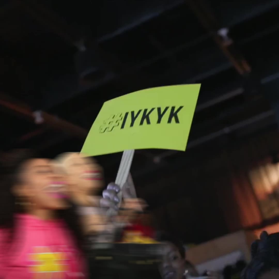An audience member holding up an IYKYK sign