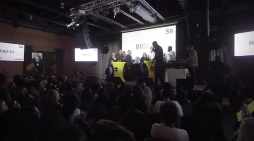 CultureTags Live! mid-game: a prompt on the big screen, players at yellow hashtag podiums, a packed room