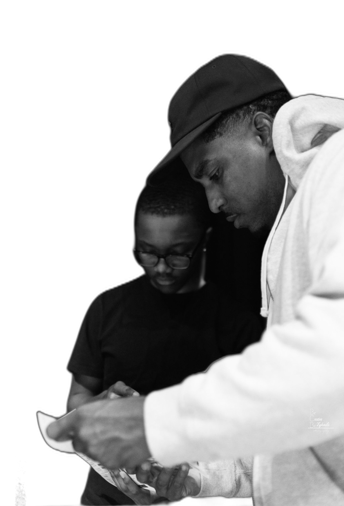 Black-and-white cutout on red: a young crew member and an adult backstage, heads bowed over a sheet of paper together
