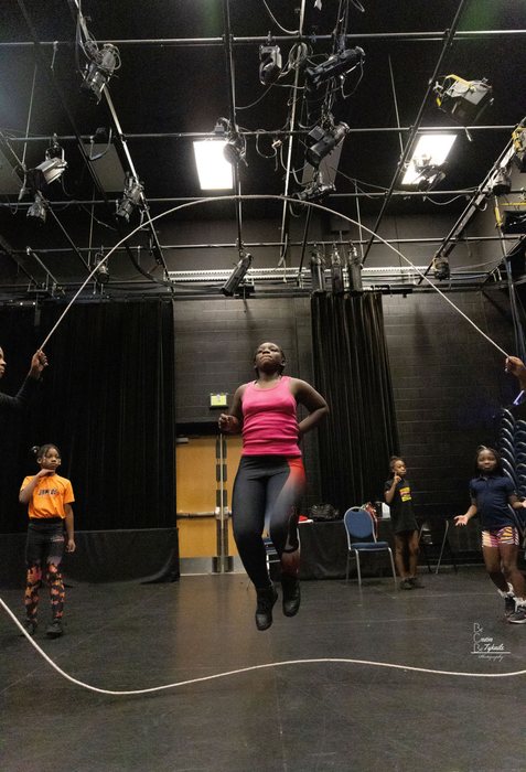 Rehearsal in a black-box studio, a performer mid-jump