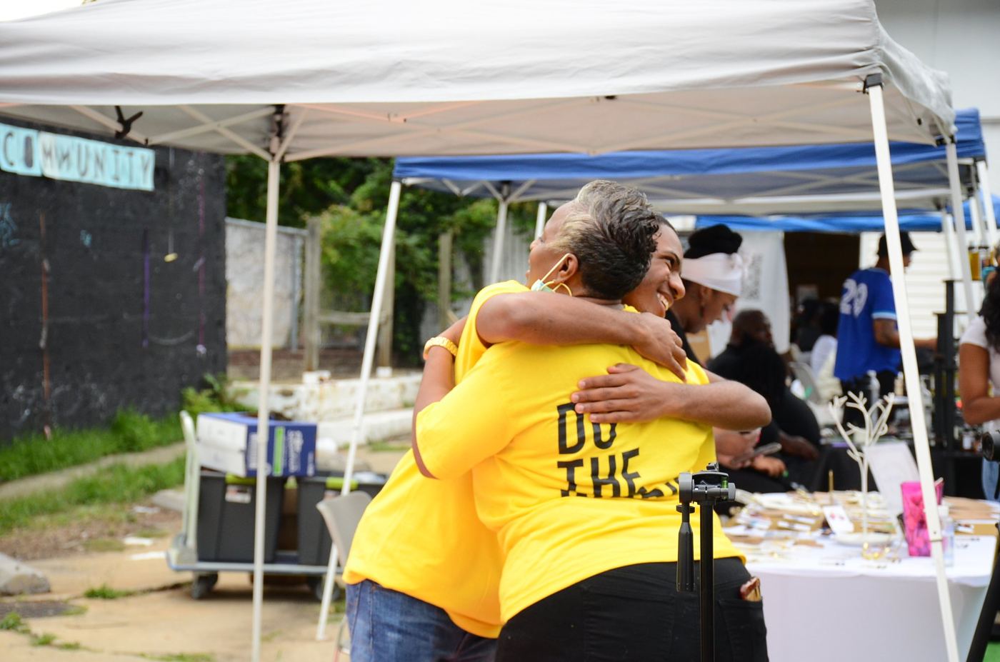Two people in DO THE WORK shirts hug under the market tents