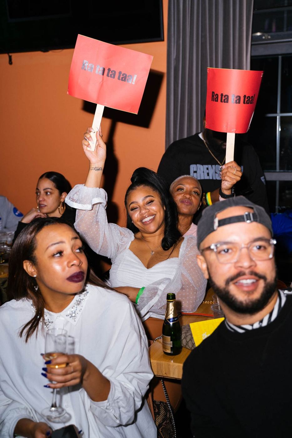 A table of guests laughing with “Ra ta ta taa!” signs held high