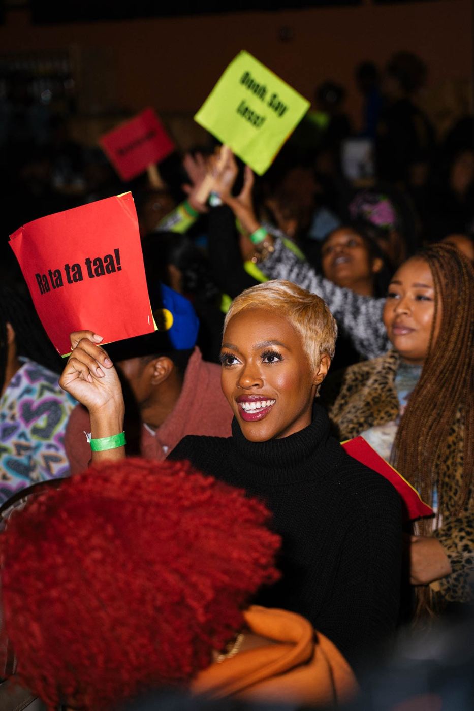 An audience member raises a “Ra ta ta taa!” sign as signs go up across the room