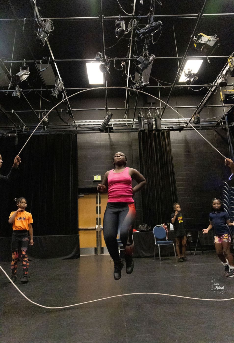 Rehearsal in the black box: a performer jumping double-dutch while the cast watches