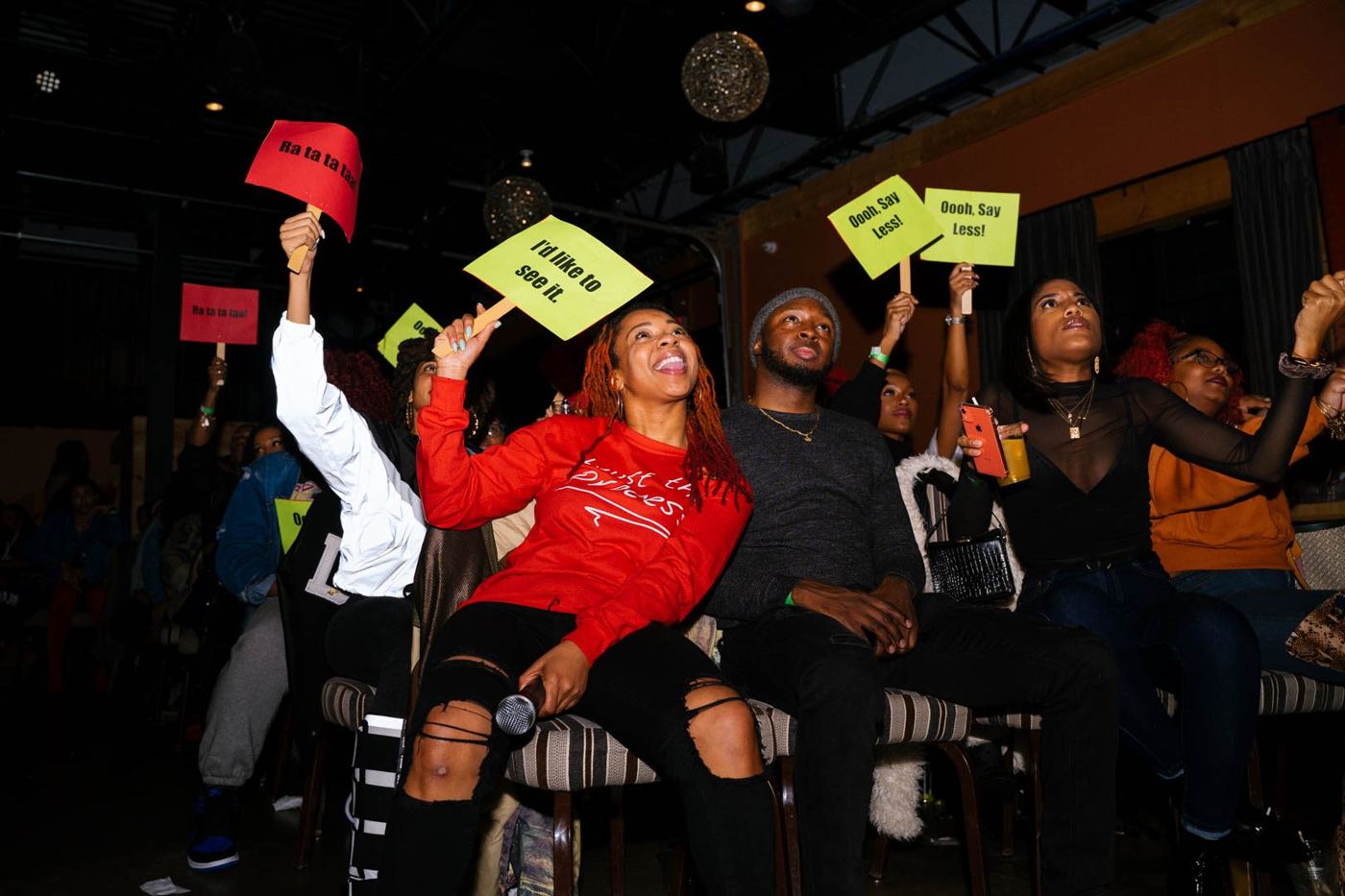 Audience members laughing and holding up reaction signs during a live show