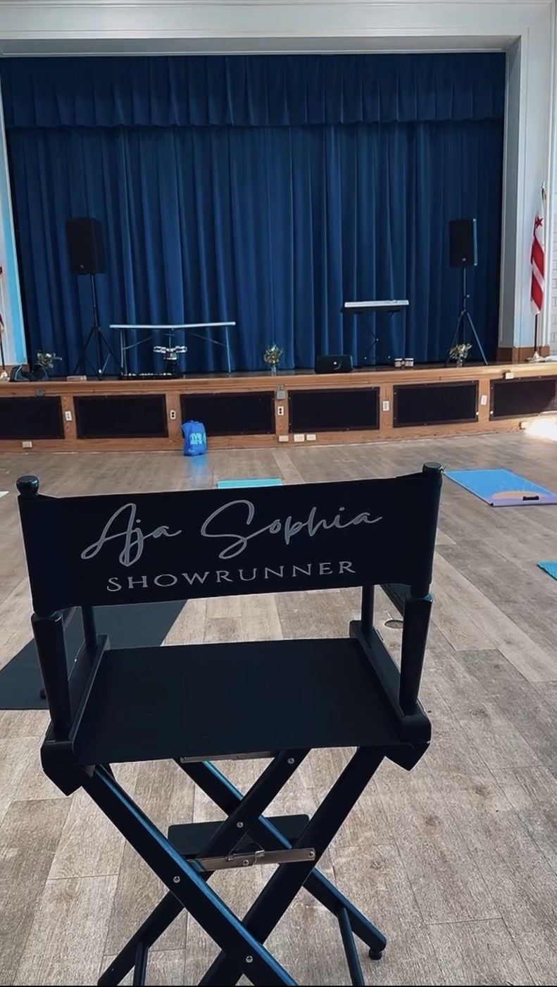 A director’s chair reading “Aja Sophia · Showrunner” in front of a stage