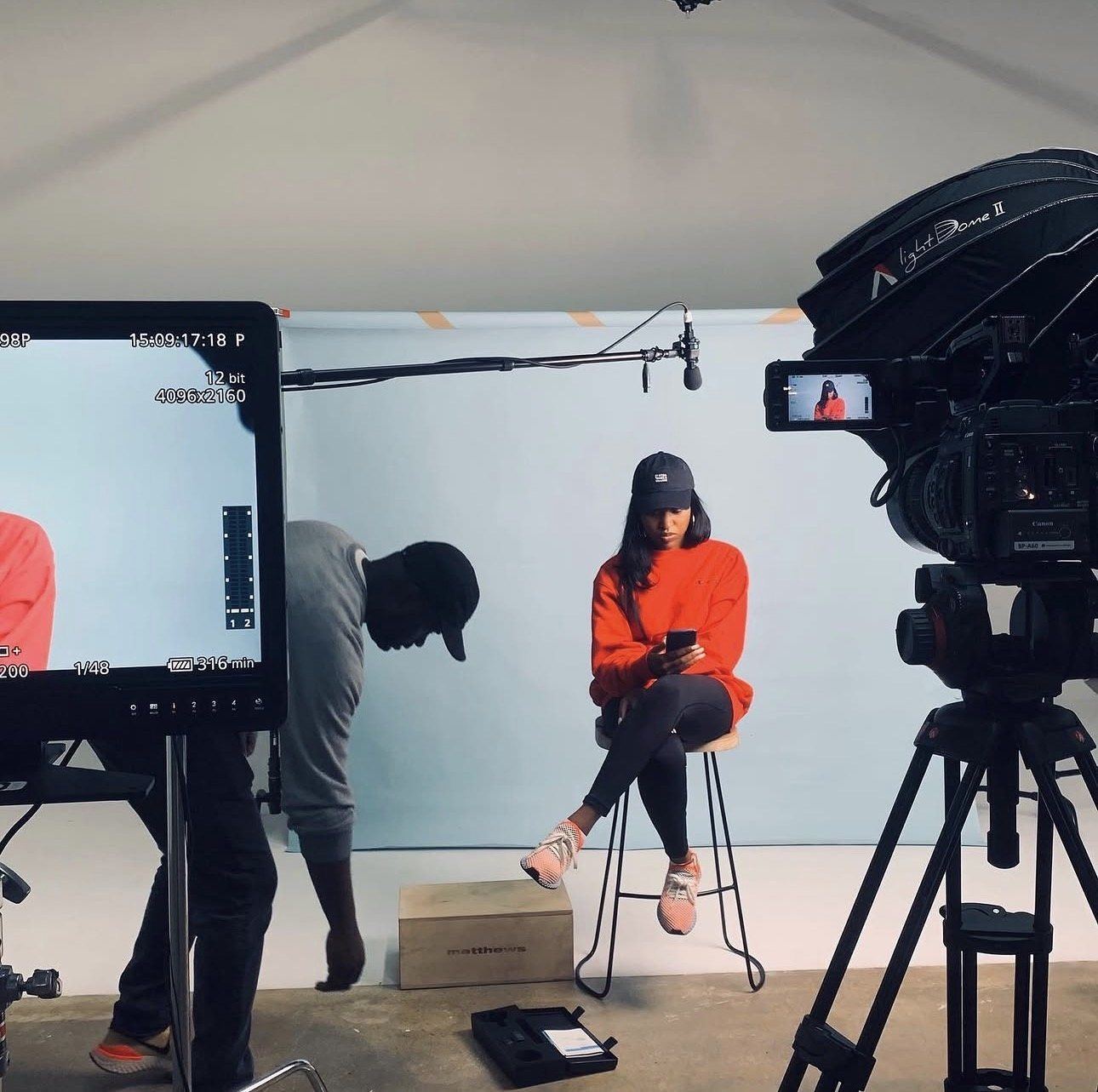 A production crew at work on a studio shoot: monitor, boom mic and camera framing a subject on a stool